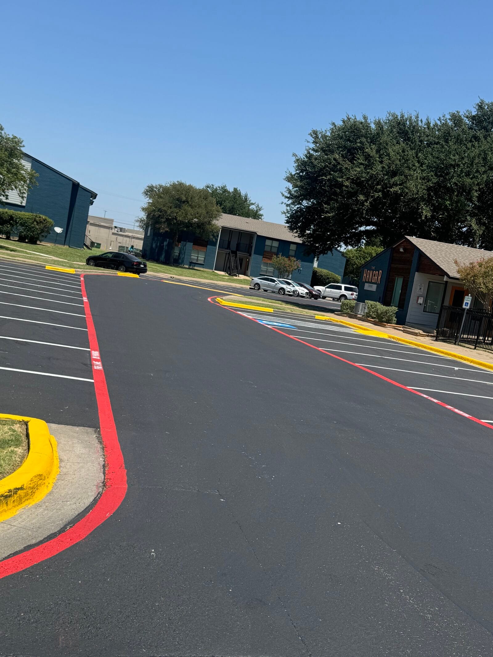 Fresh black asphalt seal coat with white stalls and red fire lanes at a Cedar Hill apartment community