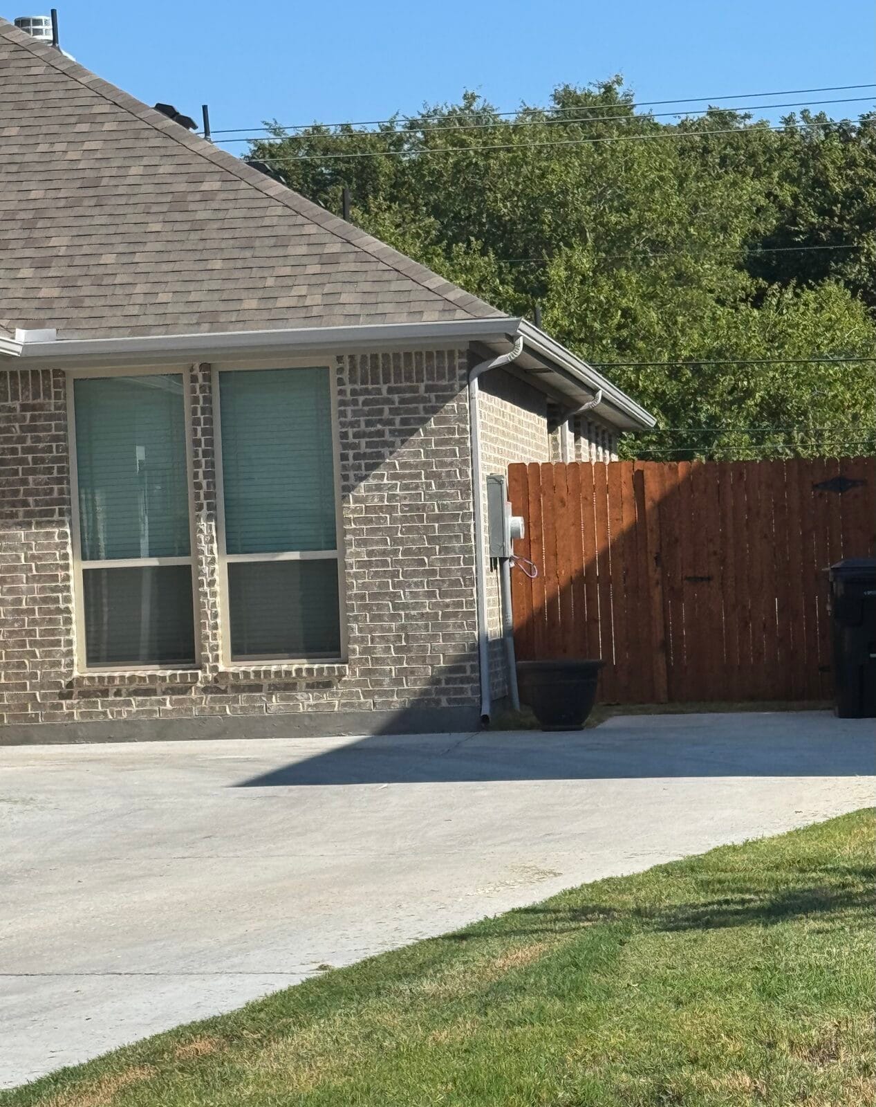 Newly installed concrete driveway running alongside a brick home to the back fence in Dallas TX
